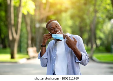 End Of Coronavirus Pandemic. Happy African American Guy Taking Off His Protective Mask At Summer Park