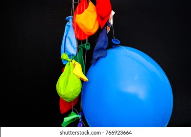 End Of A Party. Some Burst, Deflated Balloons And One Inflated Balloon Hanging On Threads. Black Background.