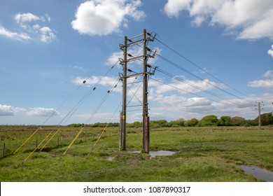 The End Of The Power Line Disappearing Underground From The Last Pylon In The Chain. Rural Power Line In A Wet Field Close To The Sea.