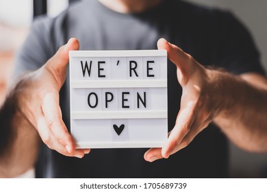 End of quarantine. Man holding lightbox with greeting text message We're open in his hands. Hotel, cafe, local shop, service owner welcoming guests after coronavirus outbreak and people shutdown. - Shutterstock ID 1705689739