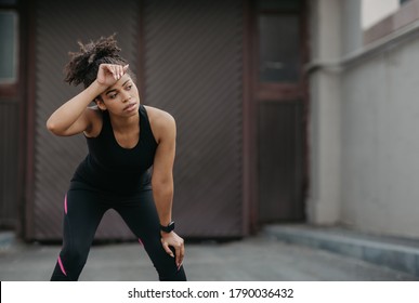 End of race. Tired african american girl in sportswear with fitness tracker wipes sweat from forehead on street after workout, outside, copy space - Powered by Shutterstock