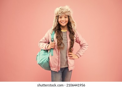 The End Of School Year. No More Exams. Small Happy Girl Back To School. Winter Holiday And Vacation. Kid Warm Clothes Pink Background. Happy Child Earflap Hat. Schoolgirl With Backpack Go Home