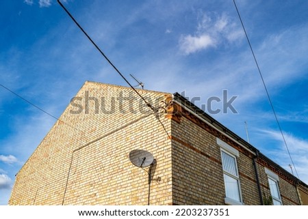 End of terraced house seen against a blue sky with a satellite disk and multiple utility cables feeding the terraced houses.