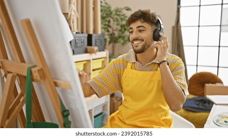 Endearing scene of a bearded young arab man, confident artist, eagerly drawing and painting on his canvas at the city's art studio, cheerfully listening to his favorite music. - Powered by Shutterstock