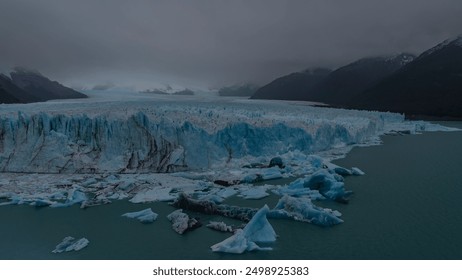 An endless field of blue ice stretches to the horizon. Cracks, sharp peaks. Melted ice floes float in the turquoise water of a glacial lake. Coastal mountains in clouds and fog. Perito Moreno. - Powered by Shutterstock