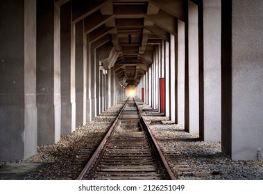 Endless rails in central perspective between close standing concrete pillars with light in vanishing point of perspective, composite