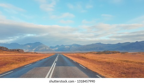 An Endless Road Leading To The Mountain Side. Colors Of Autumn. Road Is Empty, No Car Passing By. Grass On The Sides Of The Road Is Golden. Wilderness And Loneliness. Road Less Traveled.
