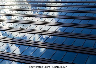 Endless rows of identical gray Windows of a modern glass office building-a skyscraper which reflects the blue sky and white clouds
