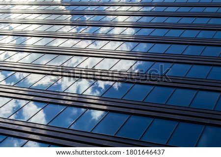 Endless rows of identical gray Windows of a modern glass office building-a skyscraper which reflects the blue sky and white clouds