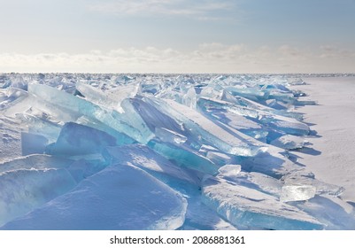 An Endless Snow-covered Field With Transparent Blue Ice Floes On Ice Hummocks On A Frosty Sunny Day. Natural Cold Background. Winter Landscape Of Frozen Siberian Lake Baikal In Cold January Weather