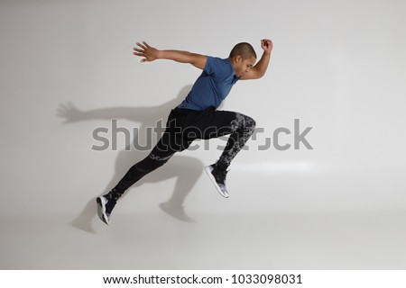 Endurance and stamina. Side view of athletic young Afro American sportsman training in studio, doing high jumps. Action shot of serious determined dark skinned male in sportswear jumping at white wall