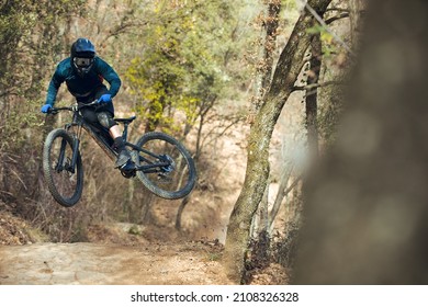 Enduro Mtb Rider Jumping Down The Mtb Track By Bikepark In The Mountains Of The Pyrenees In Catalonia. With Full Face Helmet, Goggles, Cycling Gear And Winter Protections.