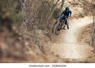Enduro mtb rider jumping down the mtb track by bikepark in the mountains of the Pyrenees in Catalonia. With full face helmet, goggles, cycling gear and winter protections.