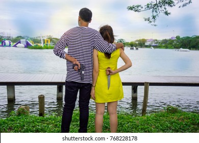 Enemy Couple, Unfaithful Lover, Affair Family, Cheating Husband And Wife, Man Holding Woman Shoulder Looking Forward But Both Hide Holding Gun And Knife Behind. Love Hate Relationship Concept.