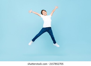 Energetic Asian mixed race boy jumping and raising hands up in isolated light blue color studio background