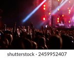 Energetic audience enjoys night music fest, illuminated stage with performers. Fans raise hands, dance in concert atmosphere. Live event entertainment, outdoor celebration, youthful excitement.