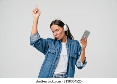 Energetic caucasian young woman girl dancing singing listening to the music podcast song singer sound track e-book in headphones earphones on cellphone isolated in white background