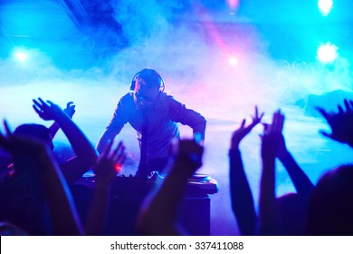 Energetic deejay standing in front of dancing people in club