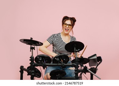 Energetic Eccentric Lady Playing On Electric Drums. Her Hair In Buns. Over Pink Background. Grimacing, Looking In The Camera.