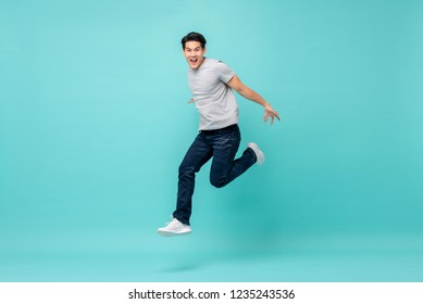 Energetic happy young Asian man in casual clothes jumping, studio shot isolated in light blue background
