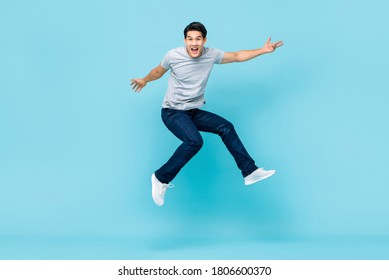 Energetic Happy Young Asian Man In Casual Clothes Jumping Studio Shot Isolated In Light Blue Background