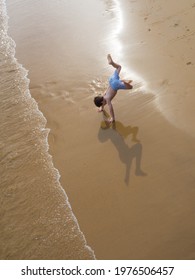Energetic little boy child doing a cartwheel or hand stand on the beach on grainy sand.