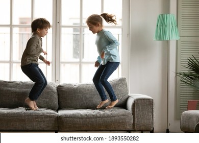 Energetic Little Kids Siblings Jumping Barefoot On Couch, Enjoying Spending Free Weekend Leisure Time Together At Home. Happy Small Preschool Brother And Sister Involved In Funny Domestic Activity.