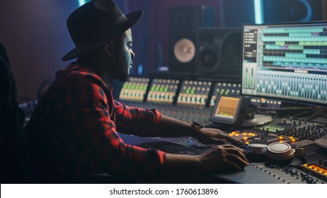 Energetic Male Audio Engineer / Producer Working in Music Recording Studio, Mixing Tracks on Control Desk and Software to Create Hit Song Track. Artist Musician Enter His Studio at Sits at Workdesk - Powered by Shutterstock