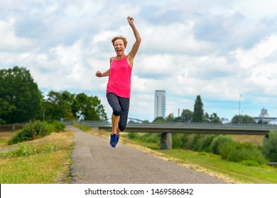 Energetic motivated exuberant middle-aged woman running along a quiet rural road leaping and cheering as she laughs at the camera in a low angle view - Shutterstock ID 1469586842