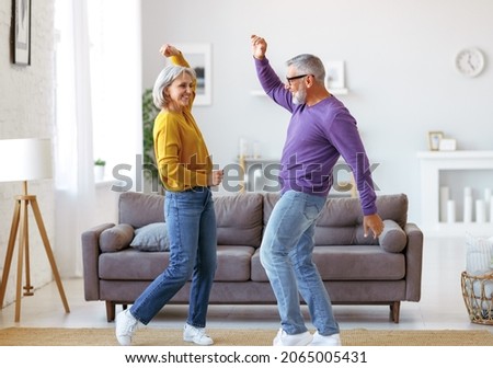
Energetic senior family couple dancing together in living room at home, moving to music and smiling, positive retired people wife and husband enjoying active life on retirement

