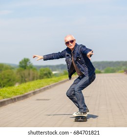 Energetic Senior Man Enjoying Riding A Skateboard. The Concept Of Life Satisfaction. Portrait Of A Positive Gray-haired Man With A Skateboard. Winner Concept.