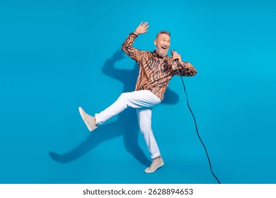 Energetic Senior Man Singing on Blue Background with Fun Dance Pose and Microphone