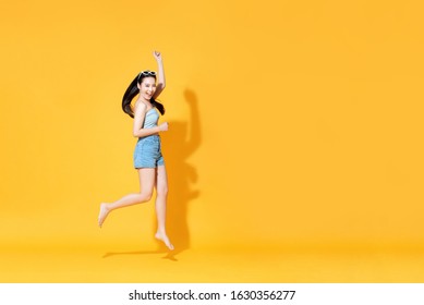 Energetic Smiling Beautiful Asian Woman In Summer Outfit Jumping Isolated On Yellow Background