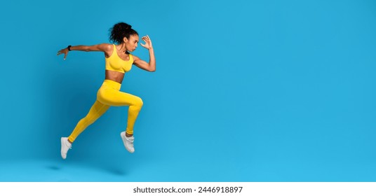 Energetic young African American woman wearing yellow sports clothing captured in a dynamic mid-air jump on a blue background - Powered by Shutterstock