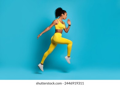 Energetic young African American woman in bright yellow sportswear captured mid-stride against a blue background - Powered by Shutterstock