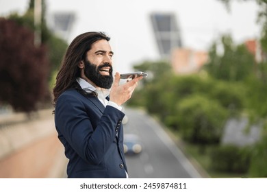 Energetic young businessman speaking into his phone using voice commands, actively engaging with technology in an urban setting. - Powered by Shutterstock