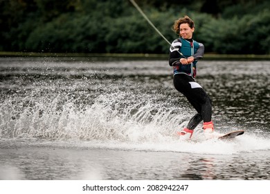 energetic young woman in wetsuit and vest rides on river water on wakeboard holding rope with her hands