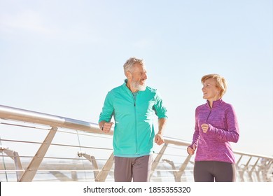 Energize Your Life. Active Mature Family Couple In Sportswear Smiling At Each Other While Running Together On A Sunny Morning. Joyful Senior Couple Working Out Outdoors