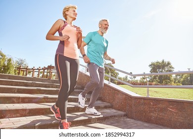 Energize Your Morning. Full Length Shot Of Active Mature Family Couple In Sportswear Running Together In The Park On A Sunny Morning. Joyful Senior Couple Working Out Outdoors