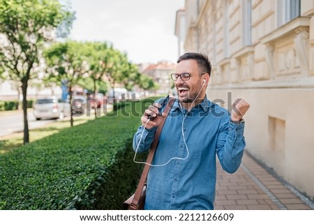 Energized adult young man with eyeglasses, jamming with his favorite music, using earphones to listen.
