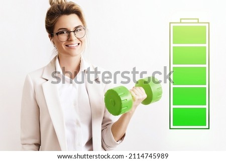 Energized business woman lifting green dumbbell. Fully charged battery symbol beside. Concepts of active life, stress free work and uplifting.