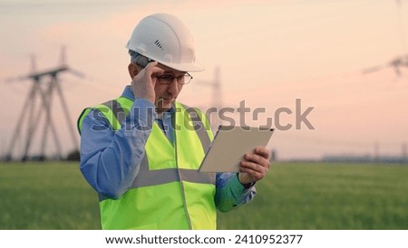 Energy business, Power engineer in safety helmet checks power line, digital tablet. Energy security, ecology. Civil engineer, specializing in electricity supply works outdoors. Modern technologies.