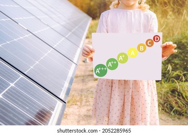 Energy Consumption Labeling Scheme. Solar Power And Energy Efficiency Concept. Girl Child Standing Next To Home Solar Farm With Help Reduce Electricity Cost.