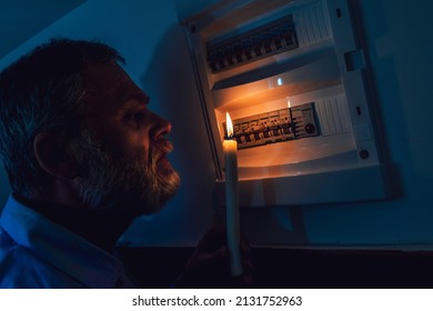 Energy crisis. Man in complete darkness holding a candle to investigate a home fuse box during a power outage. Blackout concept.