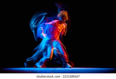 Energy. Dynamic portrait of stylish man and girl dancing hip-hop in sportive style clothes on dark background at dance hall in mixed neon light. Youth culture, hip-hop, movement, style and fashion - Powered by Shutterstock