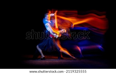 Energy. Dynamic portrait of young ballroom dancers dancing Argentine tango isolated on dark background with neon mixed light. Concept of art, beauty, grace, action, emotions. Copy space for ad