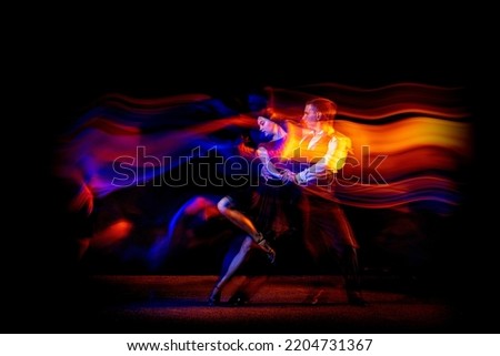 Energy. Dynamic portrait of young ballroom dancers dancing Argentine tango isolated on dark background with neon mixed light. Concept of art, beauty, grace, action, emotions. Copy space for ad