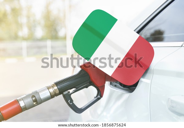 Energy and economy\
concept. Flag of Italy on the car\'s fuel filler flap with gas pump\
nozzle in the tank.