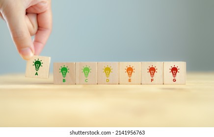 Energy efficiency and home improvement concept. Ecological and bio energetic house. Energy class;house efficiency rating. Low energy to save money. Hand holds wooden cubes with energy efficiency scale - Shutterstock ID 2141956763
