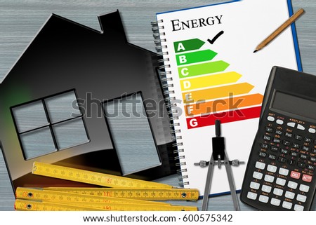 Energy efficiency rating graph in a notebook on a desk with a model house, calculator, wooden folding ruler, drawing compass and a pencil